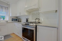 White shaker cabinetry, light-toned countertops, white subway tile backsplash, stainless steel range, and farmhouse-style sink - 