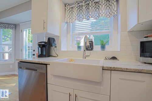 White shaker cabinetry, farmhouse sink, stainless steel dishwasher, light-toned countertop, and white subway tile backsplash - 12 Douziech Close, St. Albert, AB - Indoor Photo Showing Kitchen