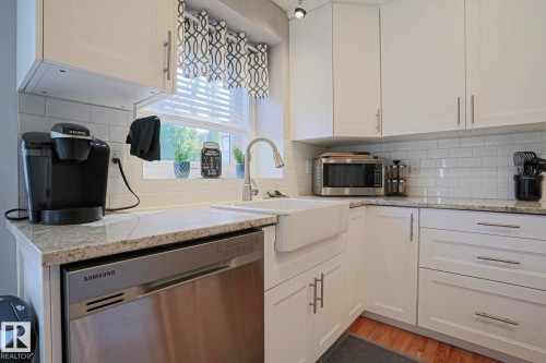 White shaker-style cabinetry with brushed nickel hardware, white subway tile backsplash, farmhouse sink with gooseneck faucet, light-toned granite countertops, and stainless steel dishwasher - 12 Douziech Close, St. Albert, AB - Indoor Photo Showing Kitchen