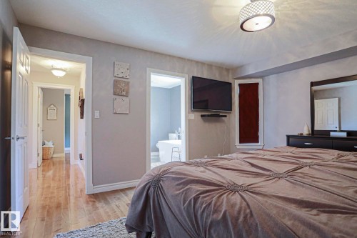 Hardwood-style flooring extends through the doorway, complemented by a contemporary ceiling light fixture - 12 Douziech Close, St. Albert, AB - Indoor Photo Showing Bedroom