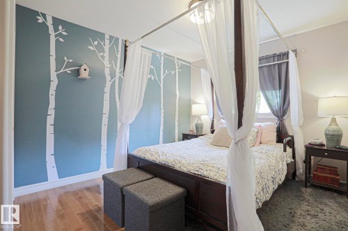 Wood-finish flooring with light-toned wall paint and an accent wall featuring tree graphics - 12 Douziech Close, St. Albert, AB - Indoor Photo Showing Bedroom