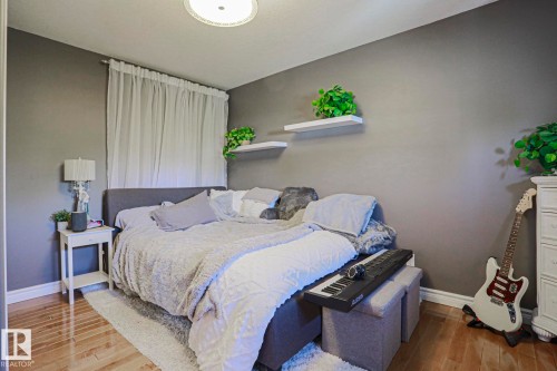 Hardwood-style flooring, neutral wall tones, window with sheer drapery, flush mount ceiling light, and white floating wall shelves - 12 Douziech Close, St. Albert, AB - Indoor Photo Showing Bedroom