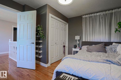 Wood-finish flooring with white baseboards, a white paneled door, and bi-fold closet doors - 12 Douziech Close, St. Albert, AB - Indoor Photo Showing Bedroom