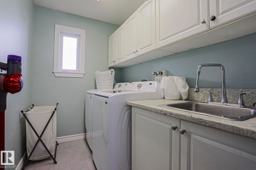 Integrated laundry area featuring white shaker-style cabinetry, a built-in stainless steel sink, and a speckled countertop - 12 Douziech Close, St. Albert, AB - Indoor Photo Showing Laundry Room
