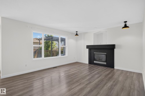 Bright interior with wood-finish flooring and a contemporary black fireplace - 1315 Westerra Drive, Stony Plain, AB - Indoor Photo Showing Living Room With Fireplace