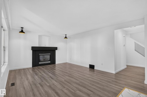 Spacious room featuring wood-finish flooring, a modern black fireplace, white walls, and contemporary overhead lighting - 1315 Westerra Drive, Stony Plain, AB - Indoor Photo Showing Living Room With Fireplace