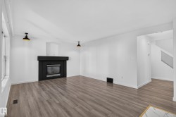 Spacious room featuring wood-finish flooring, a modern black fireplace, white walls, and contemporary overhead lighting - 