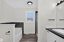 Spacious bathroom featuring a white soaking tub, dark wood-finish flooring, and a walk-in shower with black subway tile - 
