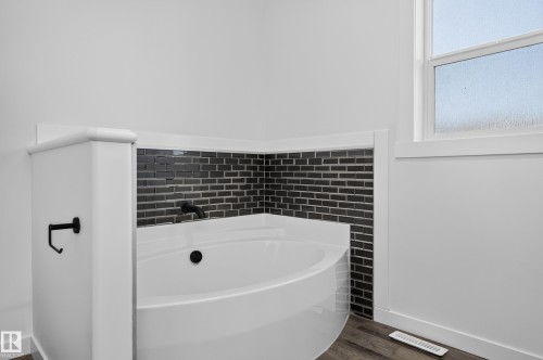 Corner soaking tub with a dark tile surround, matte black fixtures, and a privacy window - 1315 Westerra Drive, Stony Plain, AB - Indoor Photo Showing Bathroom