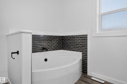 Corner soaking tub with a dark tile surround, matte black fixtures, and a privacy window - 