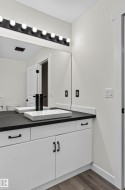 Dual vessel sinks with wall-mounted black faucets, white vanity cabinetry with black hardware, black countertop, and a large vanity mirror with a black light fixture featuring globe bulbs - 