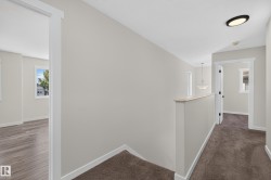 Upper-level hallway featuring neutral wall tones, contrasting white trim, and a combination of wood-finish flooring and plush carpeting - 