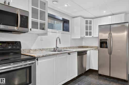 Modern kitchen featuring white cabinetry with glass-front upper cabinets, granite countertops, stainless steel appliances including a side-by-side refrigerator and dishwasher, and a black electric range - 1315 Westerra Drive, Stony Plain, AB - Indoor Photo Showing Kitchen With Double Sink