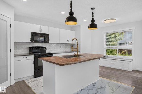 Modern kitchen featuring white cabinetry, subway tile backsplash, and a wood-finish island countertop with an integrated sink and brass-finish faucet - 1315 Westerra Drive, Stony Plain, AB - Indoor Photo Showing Kitchen