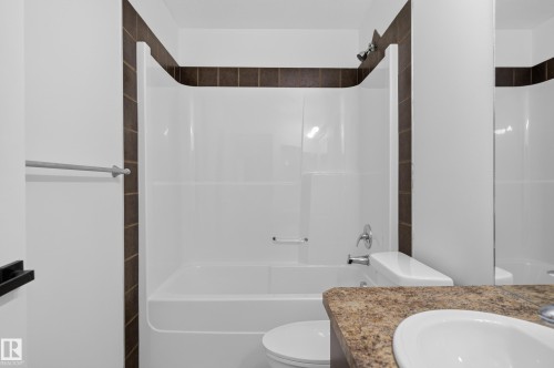 Integrated bathtub and shower combination with chrome fixtures, brown tiled surround, white toilet, and a sink with a speckled countertop - 1315 Westerra Drive, Stony Plain, AB - Indoor Photo Showing Bathroom