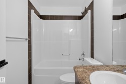 Integrated bathtub and shower combination with chrome fixtures, brown tiled surround, white toilet, and a sink with a speckled countertop - 