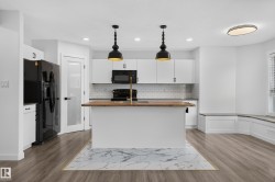 Kitchen featuring a central island with wood-finish countertop, white cabinetry, subway tile backsplash, and black appliances - 