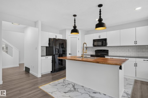 Kitchen featuring white cabinetry, black appliances, a wood-finish island countertop, a subway tile backsplash, and two pendant light fixtures - 1315 Westerra Drive, Stony Plain, AB - Indoor Photo Showing Kitchen With Double Sink