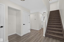 Wood-finish flooring, white paneled doors with matte black hardware, recessed lighting, and a carpeted staircase with a white handrail - 