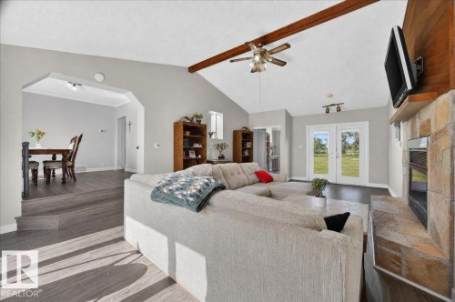 Vaulted ceiling with exposed wood beams, stone-faced fireplace with wood mantel, wood-finish flooring, and double glass panel doors to the exterior - 543069 Range Road 191, Rural Lamont County, AB - Indoor With Fireplace