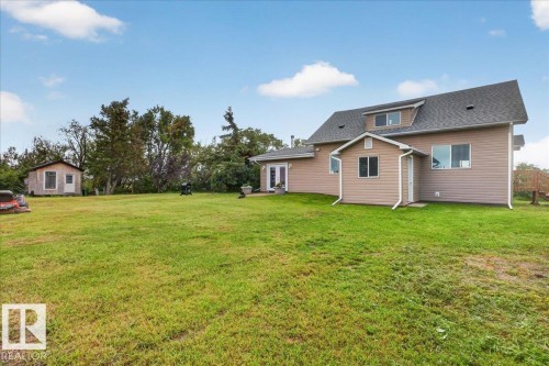 Expansive rear yard with a separate detached outbuilding, mature perimeter trees, and a two-story residence featuring dormer windows and exterior siding - 543069 Range Road 191, Rural Lamont County, AB - Outdoor