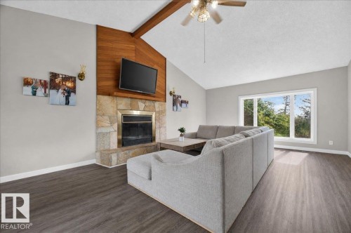 Vaulted ceiling with a ceiling fan, stone-surround fireplace with a wood mantel, wood-finish flooring, and a large multi-pane window - 543069 Range Road 191, Rural Lamont County, AB - Indoor Photo Showing Living Room With Fireplace