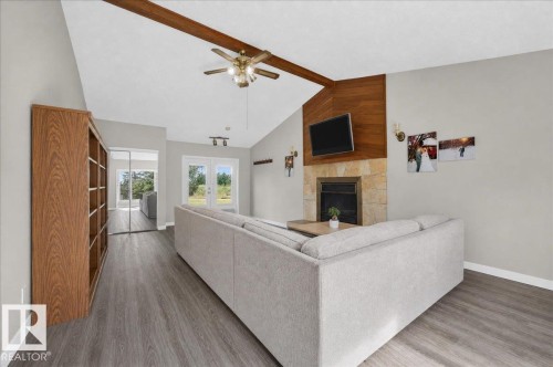 Vaulted ceiling with exposed wood beam, a stone-clad fireplace, wood-finish flooring, and double glass doors - 543069 Range Road 191, Rural Lamont County, AB - Indoor Photo Showing Other Room With Fireplace