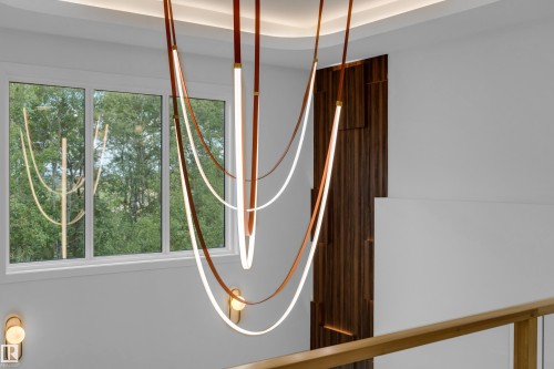 Modern multi-level chandelier, recessed ceiling lighting, wood-finish accent paneling, white window frame, and a wood-finish handrail - 2408 1 Avenue Sw, Edmonton, AB - Indoor Photo Showing Other Room
