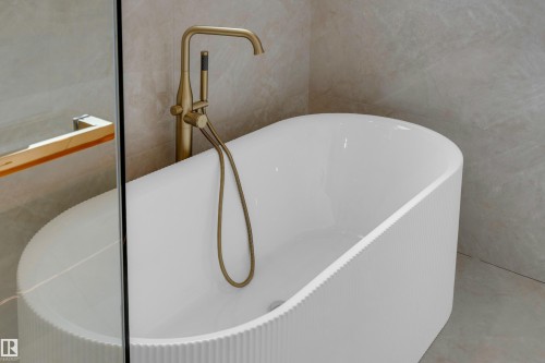 Freestanding soaking tub with a reeded exterior, accompanied by a brass floor-mounted tub filler with a hand shower - 2408 1 Avenue Sw, Edmonton, AB - Indoor Photo Showing Bathroom
