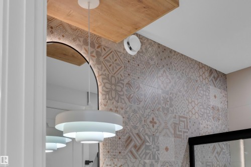 Modern entryway featuring geometric-patterned wallcovering in neutral tones, wood-finish ceiling detail, and contemporary pendant lighting with layered circular shades - 2408 1 Avenue Sw, Edmonton, AB - Indoor