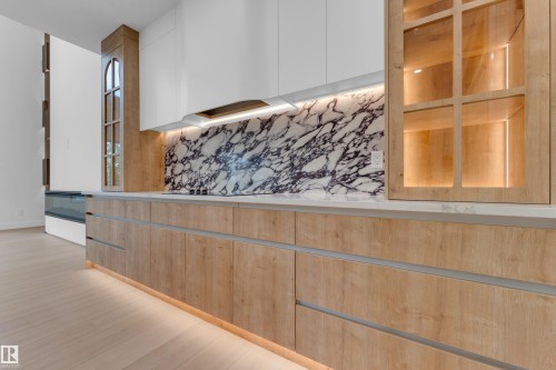 Wood-finish base cabinetry with integrated hardware, contrasting white upper cabinetry, and a full-height marble backsplash - 2408 1 Avenue Sw, Edmonton, AB - Indoor
