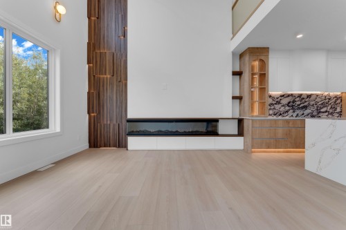 Light wood-finish flooring, accent wall with integrated lighting, electric fireplace, built-in display cabinetry, and two-story ceiling - 2408 1 Avenue Sw, Edmonton, AB - Indoor Photo Showing Other Room