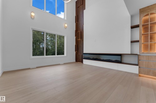 Soaring ceilings with transom windows, wood-finish flooring, linear electric fireplace, built-in display cabinetry with integrated lighting, and custom wood paneling - 2408 1 Avenue Sw, Edmonton, AB - Indoor Photo Showing Other Room