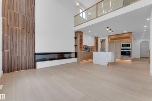Expansive open-concept living area featuring a wood-panel accent wall with integrated lighting, a linear fireplace, light wood-finish flooring, and a kitchen with an island - 2408 1 Avenue Sw, Edmonton, AB - Indoor
