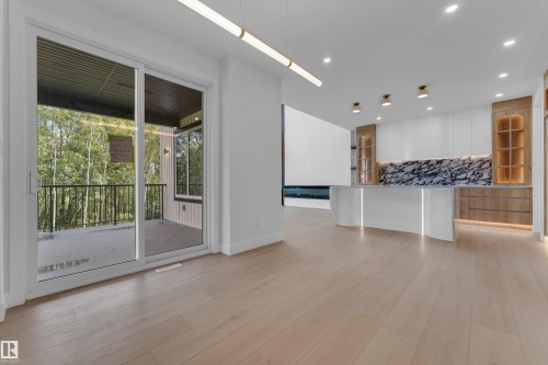 Light wood-finish flooring, sliding glass doors to outdoor balcony, modern linear lighting fixture, recessed ceiling lights, kitchen with marble-patterned backsplash, and integrated lighting - 2408 1 Avenue Sw, Edmonton, AB - Indoor Photo Showing Other Room