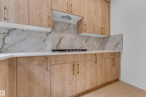 Light wood-finish cabinetry, light-toned countertops, stone-look backsplash, and a built-in cooktop - 2408 1 Avenue Sw, Edmonton, AB - Indoor Photo Showing Kitchen