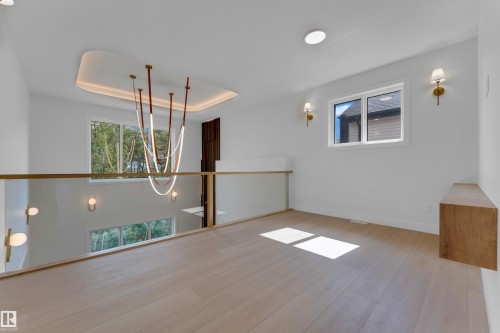 Light wood-finish flooring, glass railing with brass-finish handrail, contemporary chandeliers, recessed ceiling lighting, and multiple windows - 2408 1 Avenue Sw, Edmonton, AB - Indoor Photo Showing Other Room