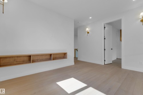 Light wood-finish flooring with a floating built-in shelf, modern wall sconces, and a white interior door with dark hardware - 2408 1 Avenue Sw, Edmonton, AB - Indoor Photo Showing Other Room