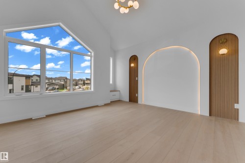 Vaulted ceiling with an architectural light fixture, expansive window, wood-finish flooring, and recessed arched wall features with integrated lighting - 2408 1 Avenue Sw, Edmonton, AB - Indoor Photo Showing Other Room