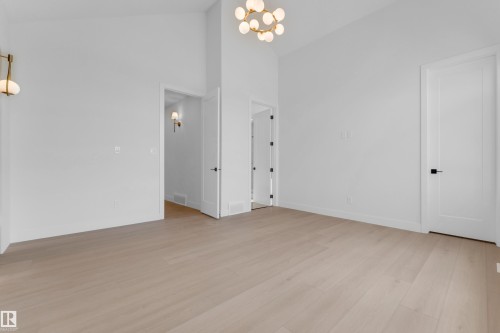 Vaulted ceiling, light wood-finish flooring, contemporary chandelier, white paneled doors, and modern sconce lighting - 2408 1 Avenue Sw, Edmonton, AB - Indoor Photo Showing Other Room
