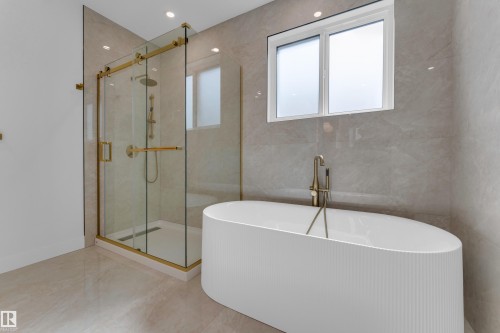 Glass-enclosed shower with gold-tone fixtures, freestanding soaking tub with floor-mounted faucet, and large-format wall and floor tile - 2408 1 Avenue Sw, Edmonton, AB - Indoor Photo Showing Bathroom