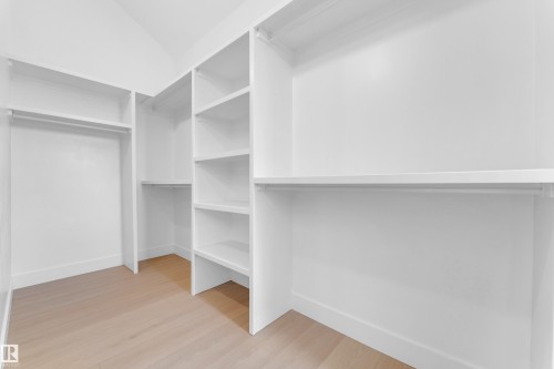 Custom built-in white shelving, integrated hanging rods, and wood-finish flooring - 2408 1 Avenue Sw, Edmonton, AB - Indoor With Storage