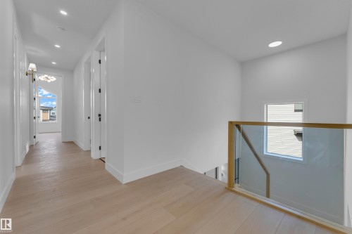 Light wood-finish flooring throughout, recessed ceiling lighting, glass and wood railing, white walls, and a decorative wall sconce - 2408 1 Avenue Sw, Edmonton, AB - Indoor Photo Showing Other Room