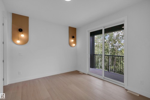 Wood-finish flooring with recessed lighting, complemented by decorative wall sconces and a sliding glass door leading to a private balcony with black metal railings - 2408 1 Avenue Sw, Edmonton, AB - Indoor Photo Showing Other Room