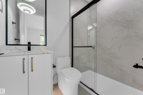 White vanity with gold-finish hardware, black-framed mirror, matte black fixtures, and a glass-enclosed shower with tiled walls - 2408 1 Avenue Sw, Edmonton, AB - Indoor Photo Showing Bathroom