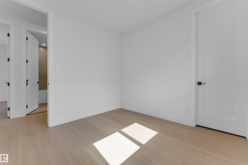 Wood-finish flooring, white walls, and modern slab doors with matte black hardware - 2408 1 Avenue Sw, Edmonton, AB - Indoor Photo Showing Other Room