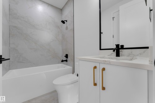 Bathroom featuring white cabinetry with gold-tone hardware, a white vessel sink with a black faucet, a white bathtub, and large format wall tiling - 2408 1 Avenue Sw, Edmonton, AB - Indoor Photo Showing Bathroom