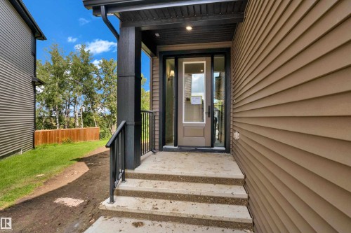Modern entry vestibule featuring a dark-framed glass storm door, concrete stepped approach, black metal railings, and siding in neutral earth tones - 2408 1 Avenue Sw, Edmonton, AB - Outdoor With Deck Patio Veranda With Exterior