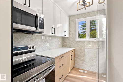 Kitchen featuring stainless steel appliances, light wood-finish cabinetry, white countertops, and a full-height tiled backsplash - 18307 66 Avenue Nw, Edmonton, AB - Indoor Photo Showing Kitchen With Upgraded Kitchen
