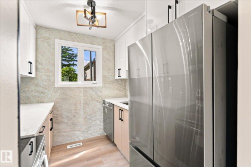 Stainless steel French door refrigerator, wood-finish flooring, white cabinetry, integrated dishwasher, and a window with exterior views - 18307 66 Avenue Nw, Edmonton, AB - Indoor